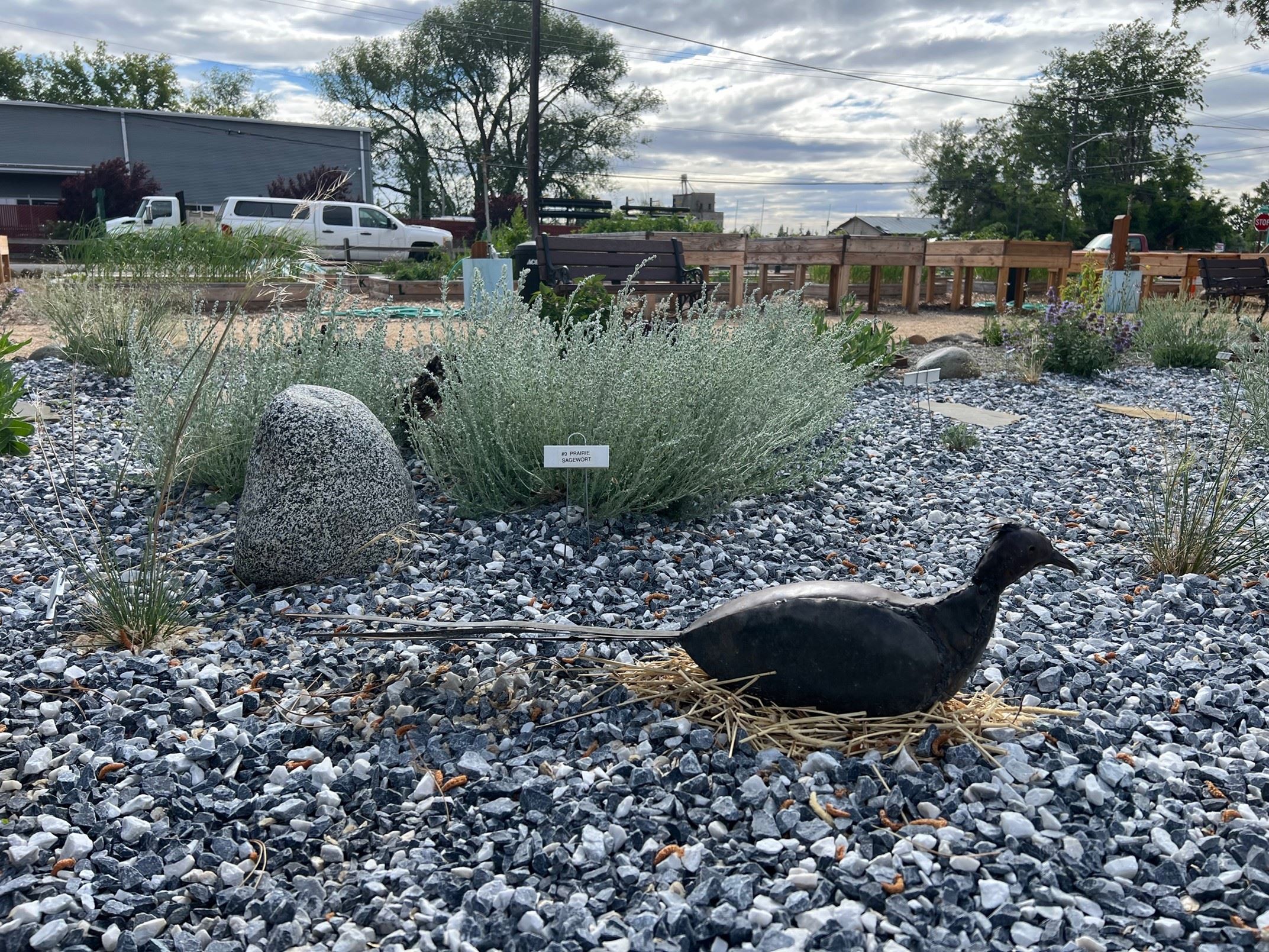 Metal artwork of a pheasant sitting on a fake nest in a rock garden.