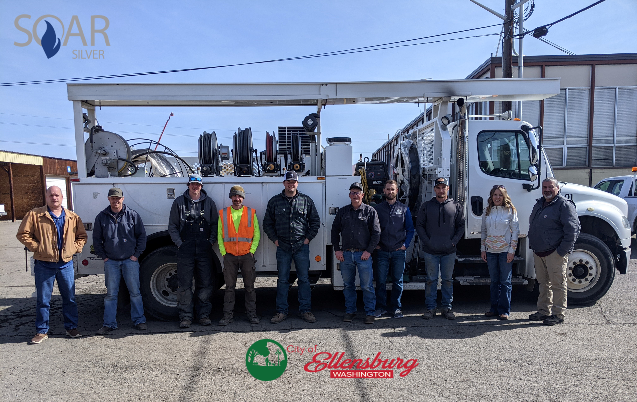 seven members of City natural gas crew standing in front of vehicle with SOAR logo in top right